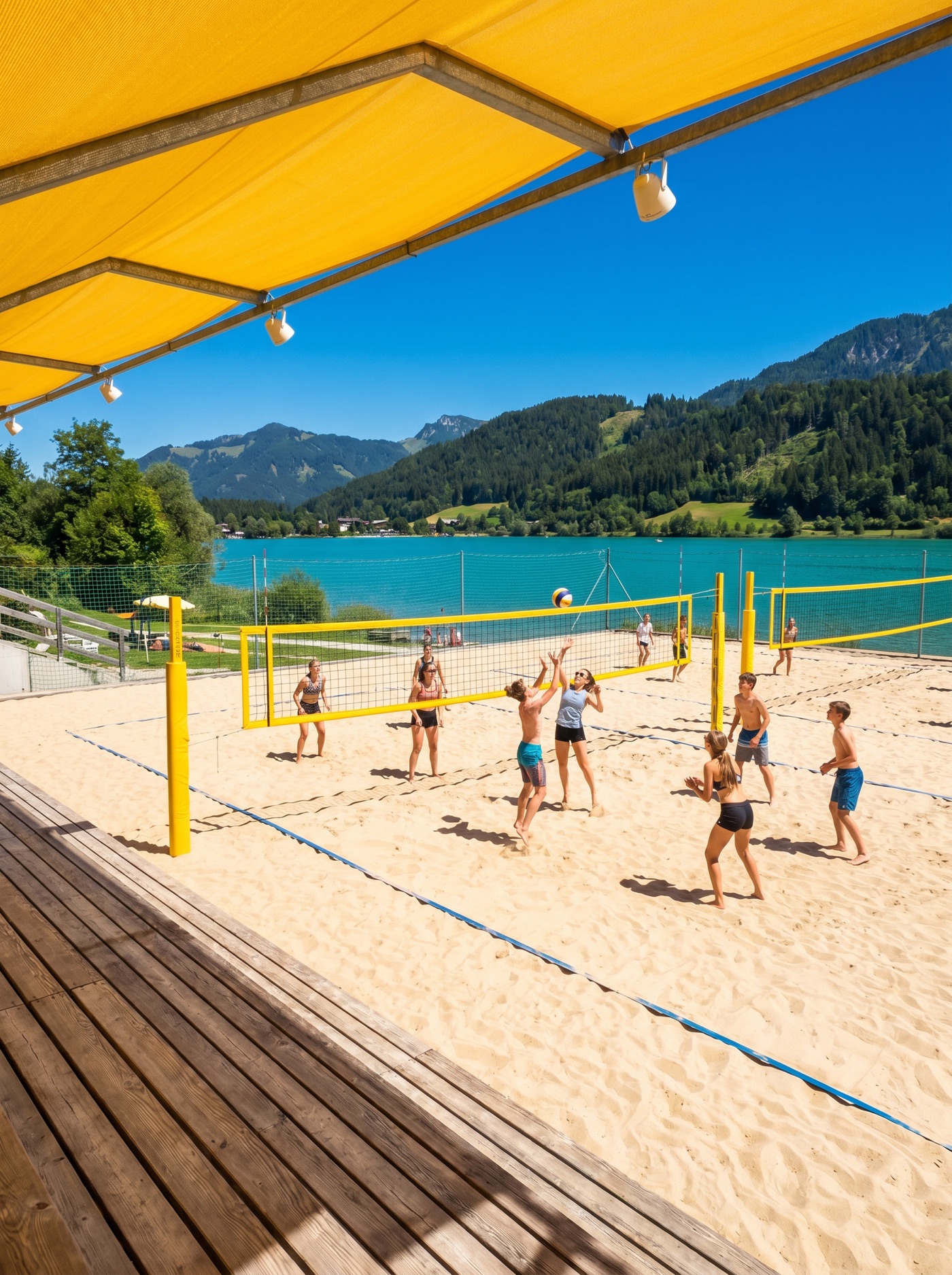 Schulklasse spielt Beachvolleyball auf sonnigen Sandplätzen mit gelben Netzen am türkisen Klopeiner See